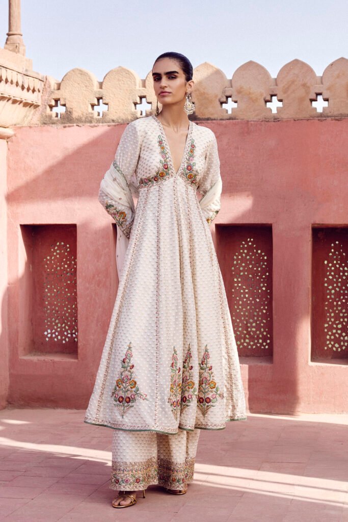Elegant ivory embroidered Anarkali suit with floral embroidery and palazzo pants worn by a woman in a heritage courtyard setting